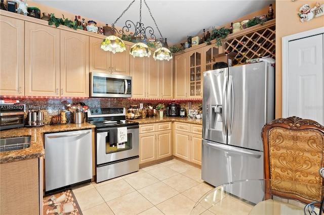 kitchen with hanging light fixtures, stainless steel appliances, light brown cabinetry, light tile patterned floors, and dark stone counters