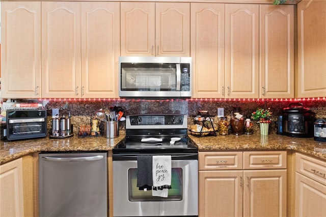 kitchen with stainless steel appliances, light brown cabinets, and dark stone countertops