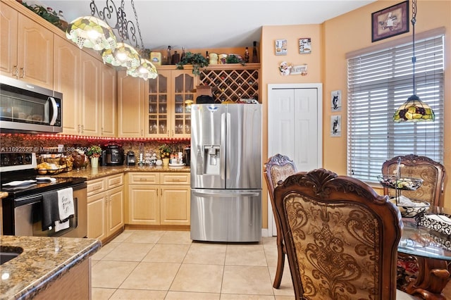 kitchen with appliances with stainless steel finishes, hanging light fixtures, light tile patterned floors, light brown cabinetry, and light stone counters