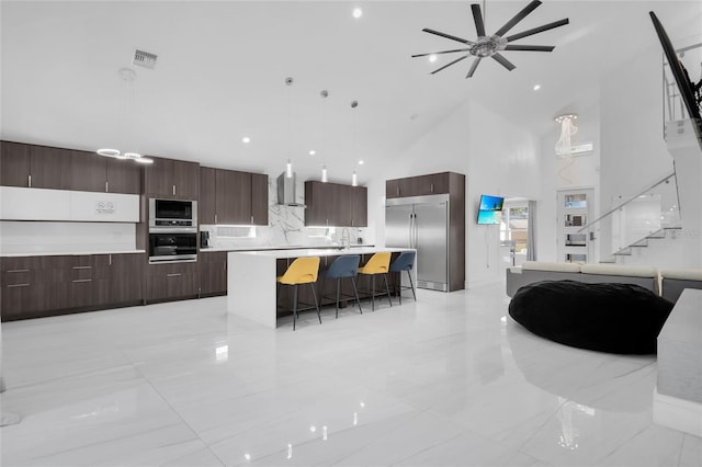 kitchen featuring wall chimney exhaust hood, high vaulted ceiling, built in appliances, pendant lighting, and a kitchen island