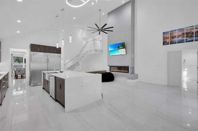 kitchen with high vaulted ceiling, a center island with sink, ceiling fan, decorative light fixtures, and dark brown cabinetry