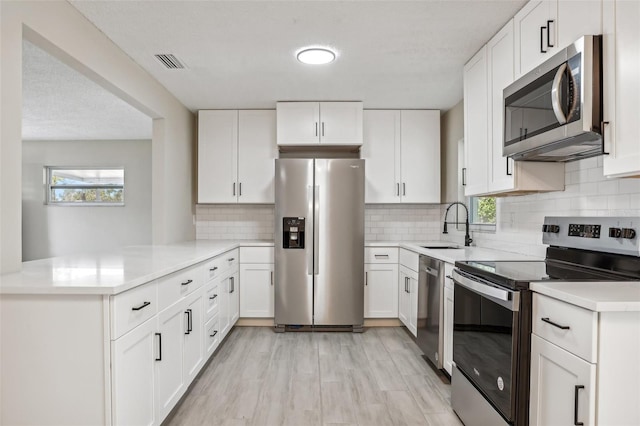 kitchen with kitchen peninsula, white cabinetry, sink, and appliances with stainless steel finishes