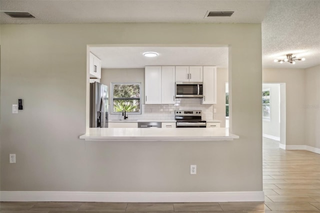 kitchen featuring backsplash, light wood-type flooring, a textured ceiling, white cabinetry, and stainless steel appliances