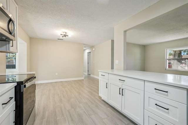 kitchen with white cabinets, appliances with stainless steel finishes, light wood-type flooring, and a textured ceiling