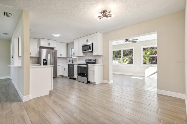 kitchen with sink, ceiling fan, light wood-type flooring, white cabinetry, and stainless steel appliances