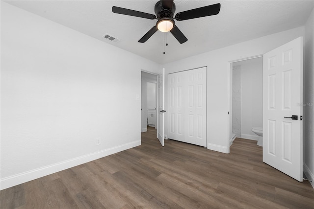 unfurnished bedroom featuring ceiling fan, ensuite bathroom, and dark wood-type flooring