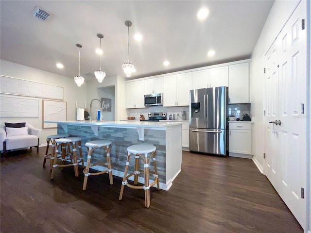 kitchen featuring dark wood-type flooring, white cabinets, hanging light fixtures, an island with sink, and stainless steel appliances