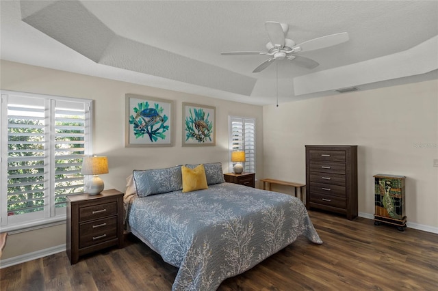 bedroom with dark wood-type flooring, ceiling fan, a raised ceiling, and multiple windows