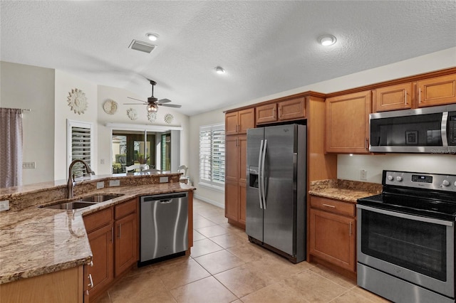 kitchen featuring sink, vaulted ceiling, light tile patterned floors, stainless steel appliances, and light stone countertops