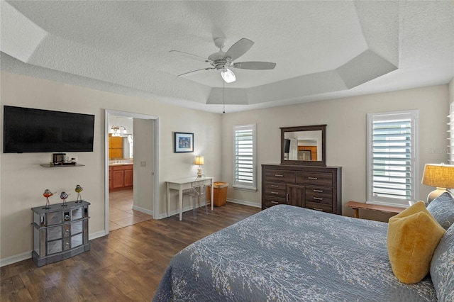 bedroom featuring dark hardwood / wood-style floors, connected bathroom, ceiling fan, a raised ceiling, and a textured ceiling