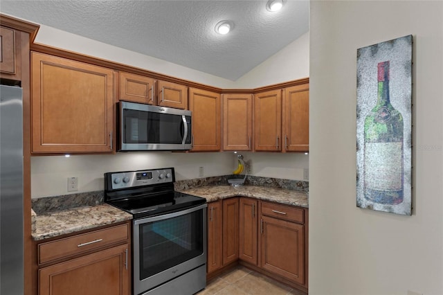 kitchen with lofted ceiling, stainless steel appliances, light tile patterned floors, and dark stone counters