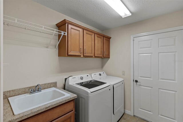 laundry area with sink, cabinets, light tile patterned floors, independent washer and dryer, and a textured ceiling