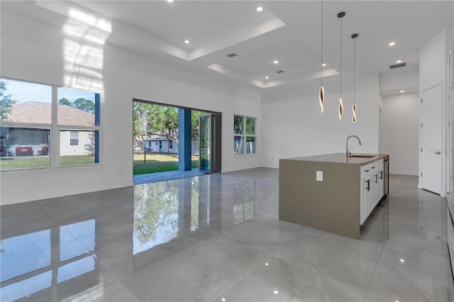 kitchen featuring white cabinets, a center island with sink, sink, a tray ceiling, and decorative light fixtures