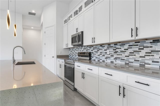 kitchen with backsplash, sink, hanging light fixtures, appliances with stainless steel finishes, and white cabinetry