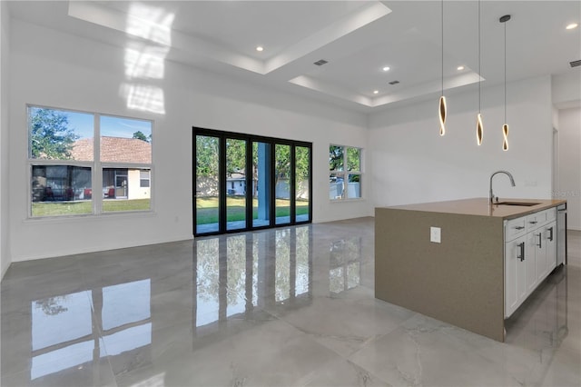 kitchen with a kitchen island with sink, sink, a tray ceiling, decorative light fixtures, and white cabinetry