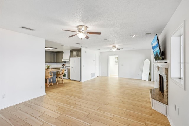 unfurnished living room with ceiling fan, a textured ceiling, and light hardwood / wood-style flooring