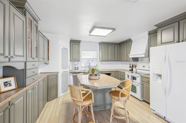 kitchen featuring light hardwood / wood-style flooring, white appliances, a kitchen bar, gray cabinets, and custom exhaust hood