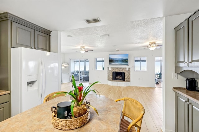 dining room featuring a premium fireplace, light hardwood / wood-style flooring, ceiling fan, and a textured ceiling