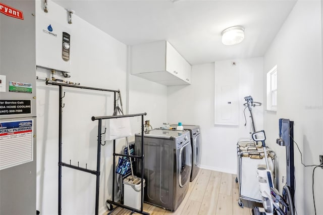 clothes washing area featuring washing machine and clothes dryer, light hardwood / wood-style flooring, and cabinets