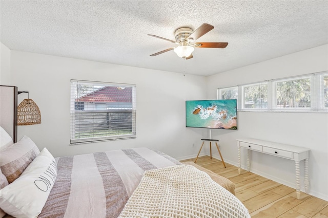 bedroom with multiple windows, wood-type flooring, a textured ceiling, and ceiling fan