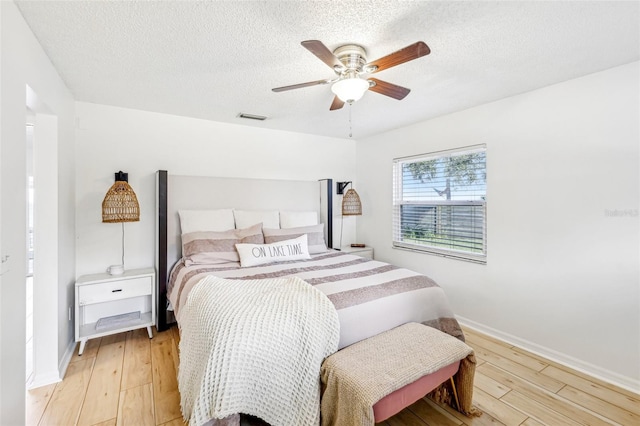 bedroom with a textured ceiling, light hardwood / wood-style flooring, and ceiling fan