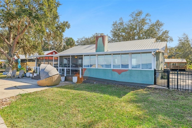 back of property with a sunroom, a patio area, and a lawn