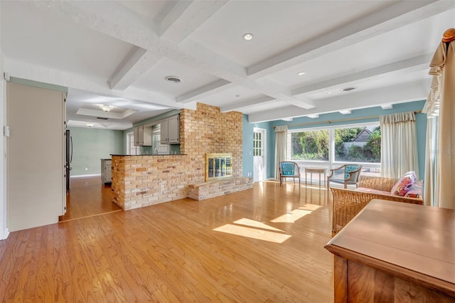 unfurnished living room with beamed ceiling, coffered ceiling, a brick fireplace, and light hardwood / wood-style flooring