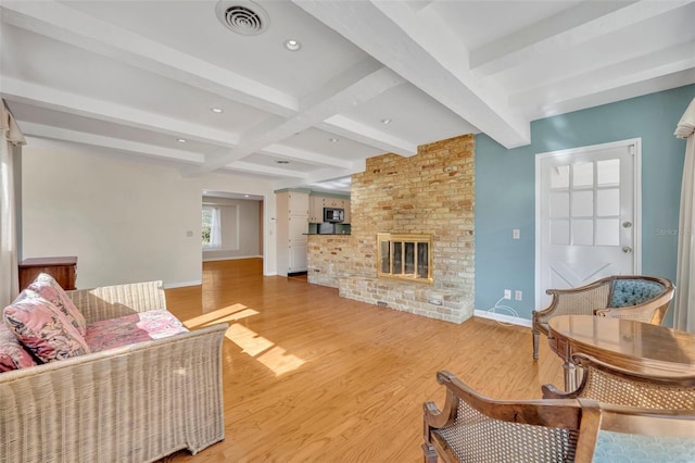 living room featuring beamed ceiling, light wood-type flooring, and a brick fireplace