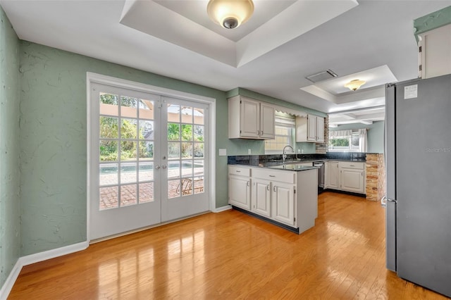 kitchen featuring french doors, white cabinets, light wood-type flooring, a tray ceiling, and stainless steel appliances