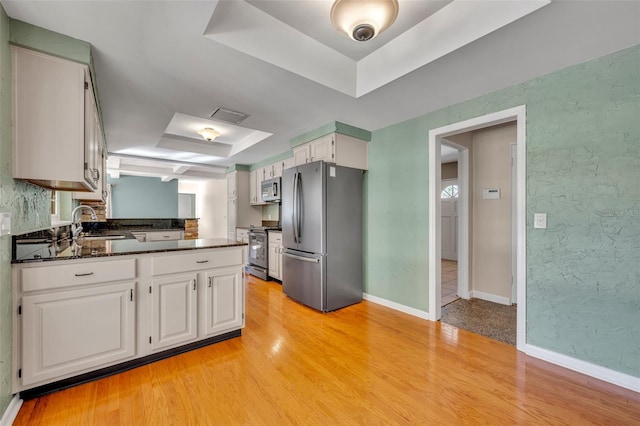 kitchen with a raised ceiling, white cabinetry, light hardwood / wood-style flooring, and stainless steel appliances