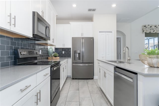 kitchen featuring sink, decorative backsplash, appliances with stainless steel finishes, light tile patterned flooring, and white cabinetry