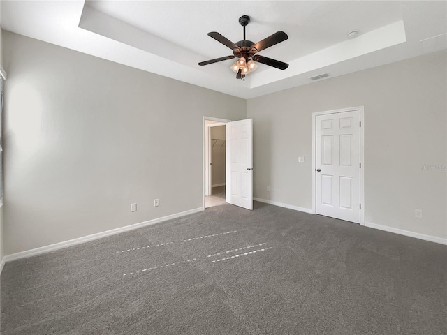 unfurnished bedroom with a raised ceiling, ceiling fan, and dark colored carpet