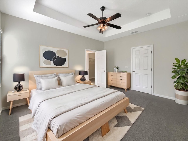 bedroom featuring a raised ceiling, ceiling fan, dark carpet, and a spacious closet