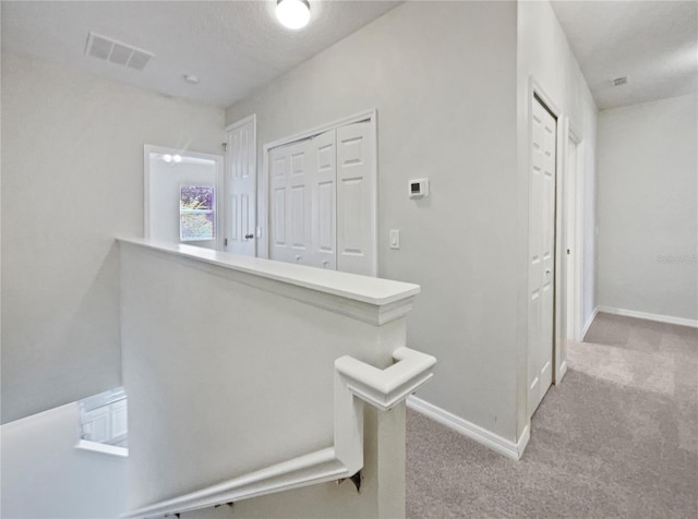 hall with baseboards, light colored carpet, and visible vents