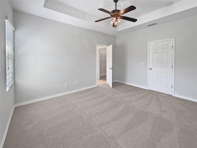 unfurnished bedroom featuring carpet flooring, a tray ceiling, baseboards, and visible vents