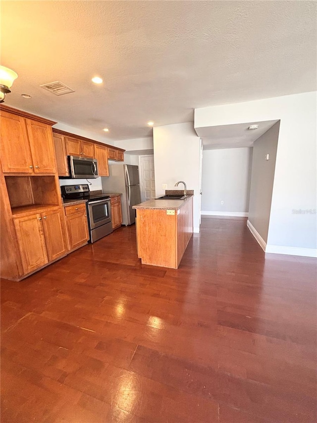 kitchen with appliances with stainless steel finishes, a textured ceiling, a center island with sink, and sink