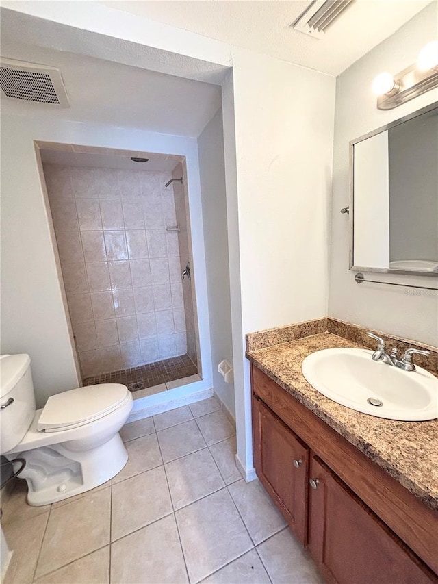 bathroom with tile patterned floors, vanity, toilet, and a tile shower