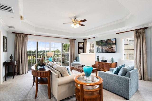 living room featuring light colored carpet, ceiling fan, a raised ceiling, and ornamental molding