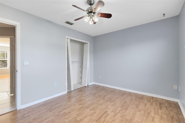 unfurnished bedroom with light wood-type flooring, a closet, a spacious closet, and ceiling fan