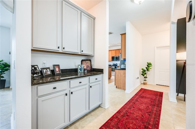 kitchen with light tile patterned flooring, appliances with stainless steel finishes, and dark stone counters