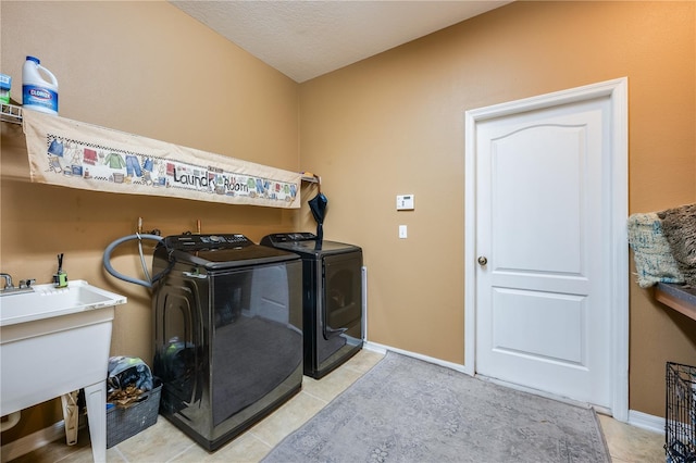 clothes washing area with light tile patterned flooring, washer and clothes dryer, sink, and a textured ceiling