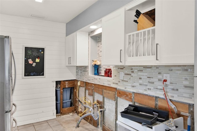 kitchen featuring light tile patterned flooring, white cabinetry, backsplash, and stainless steel refrigerator