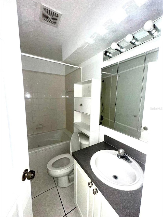 full bathroom with tile patterned floors, a textured ceiling, toilet, vanity, and tiled shower / bath