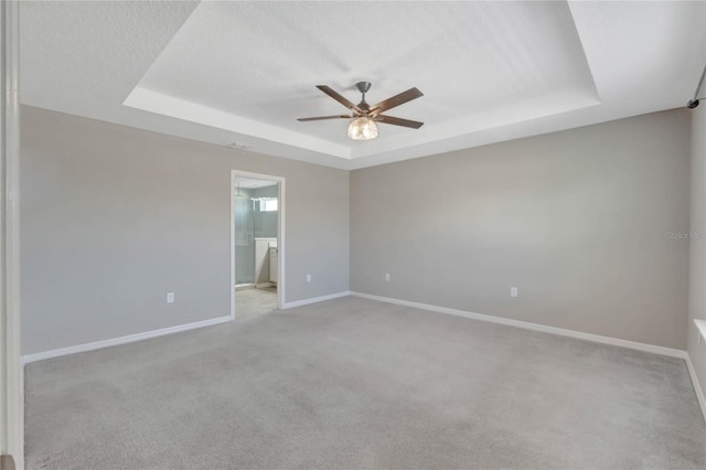 empty room with a tray ceiling, ceiling fan, and light colored carpet