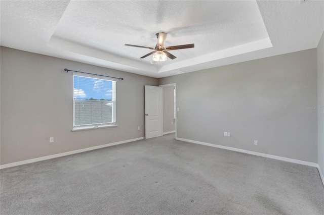 carpeted spare room with a textured ceiling, a tray ceiling, and ceiling fan