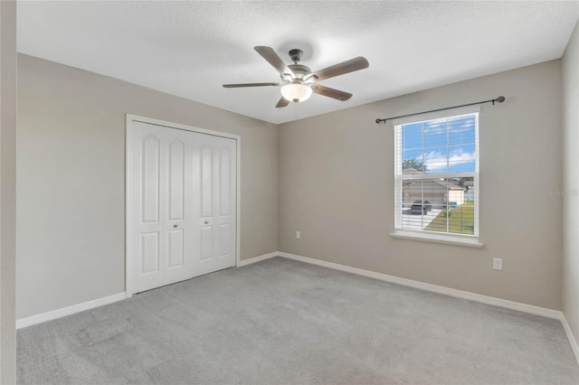 unfurnished bedroom featuring ceiling fan, a closet, light carpet, and a textured ceiling