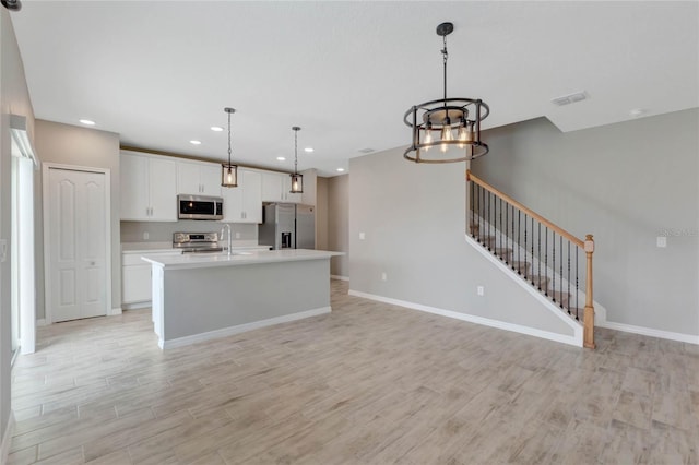 kitchen featuring a notable chandelier, decorative light fixtures, a kitchen island with sink, white cabinets, and appliances with stainless steel finishes