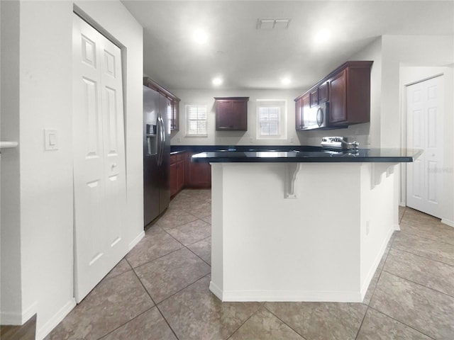 kitchen with a breakfast bar, appliances with stainless steel finishes, kitchen peninsula, and light tile patterned flooring