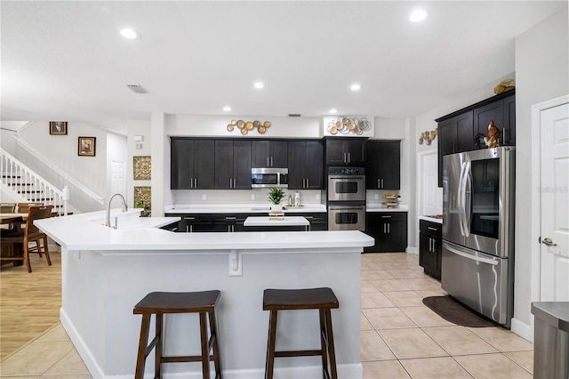 kitchen featuring appliances with stainless steel finishes, sink, light tile patterned floors, a breakfast bar area, and an island with sink