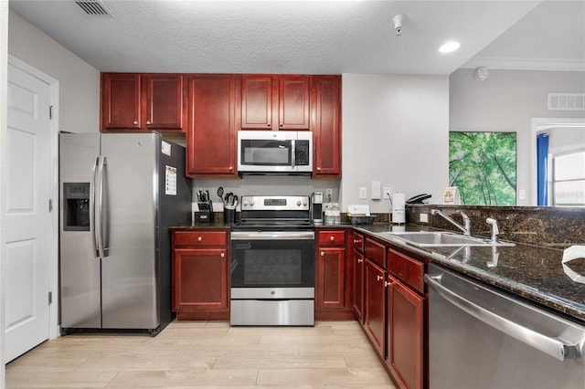 kitchen featuring dark stone counters, sink, light wood-type flooring, a textured ceiling, and stainless steel appliances